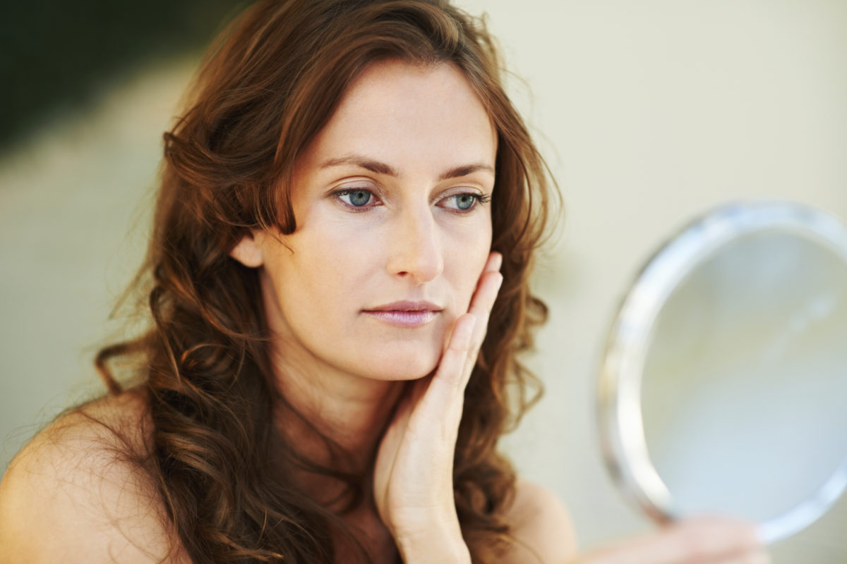 woman with hand on her cheek looking in mirror