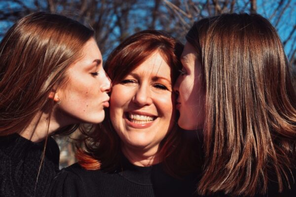 Sun shining on Mom and Daughters as they kiss her cheek